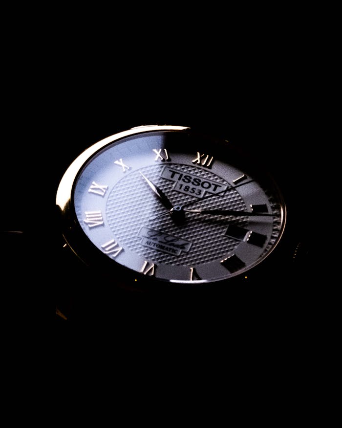 Close-up of a classic Tissot wristwatch with Roman numerals in a dark setting.